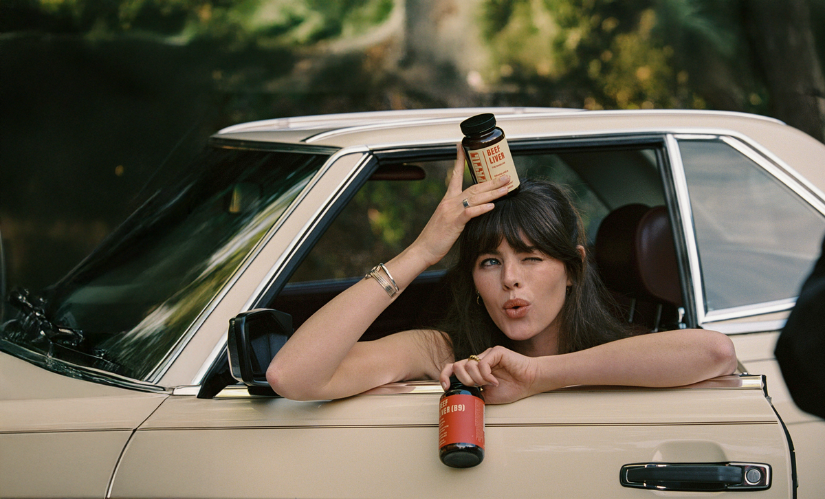 Woman leaning out of a car window holding FRTIL Beef Liver bottles