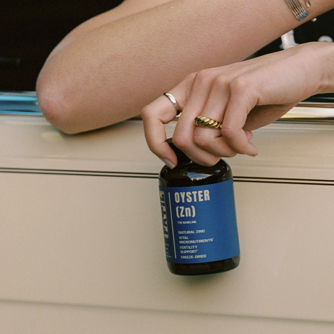 Hand holding a bottle of FRTIL Oyster (Zn), a whole-food zinc supplement made from freeze-dried oyster.