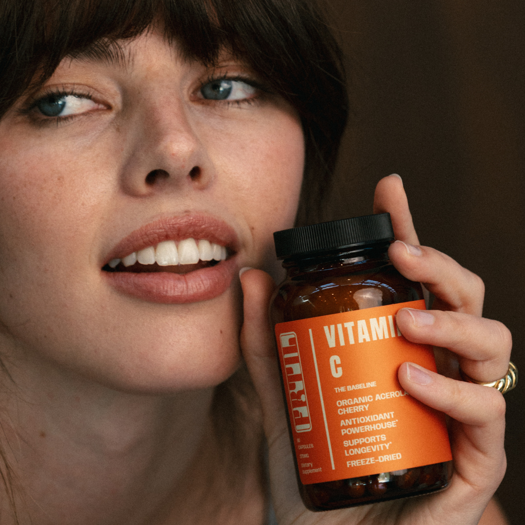 Woman holding a bottle of FRTIL organic acerola cherry vitamin C supplement in a lifestyle setting.