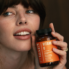 Woman holding a bottle of FRTIL organic acerola cherry vitamin C supplement in a lifestyle setting.