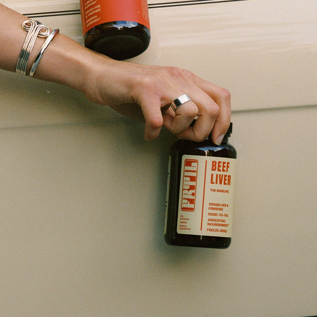 Hand holding a bottle of FRTIL grass-fed and finished beef liver supplement in a lifestyle setting.