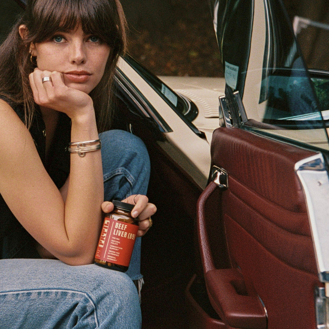 Woman holding a bottle of FRTIL Grass-Fed Beef Liver (B9) supplement in a lifestyle setting.